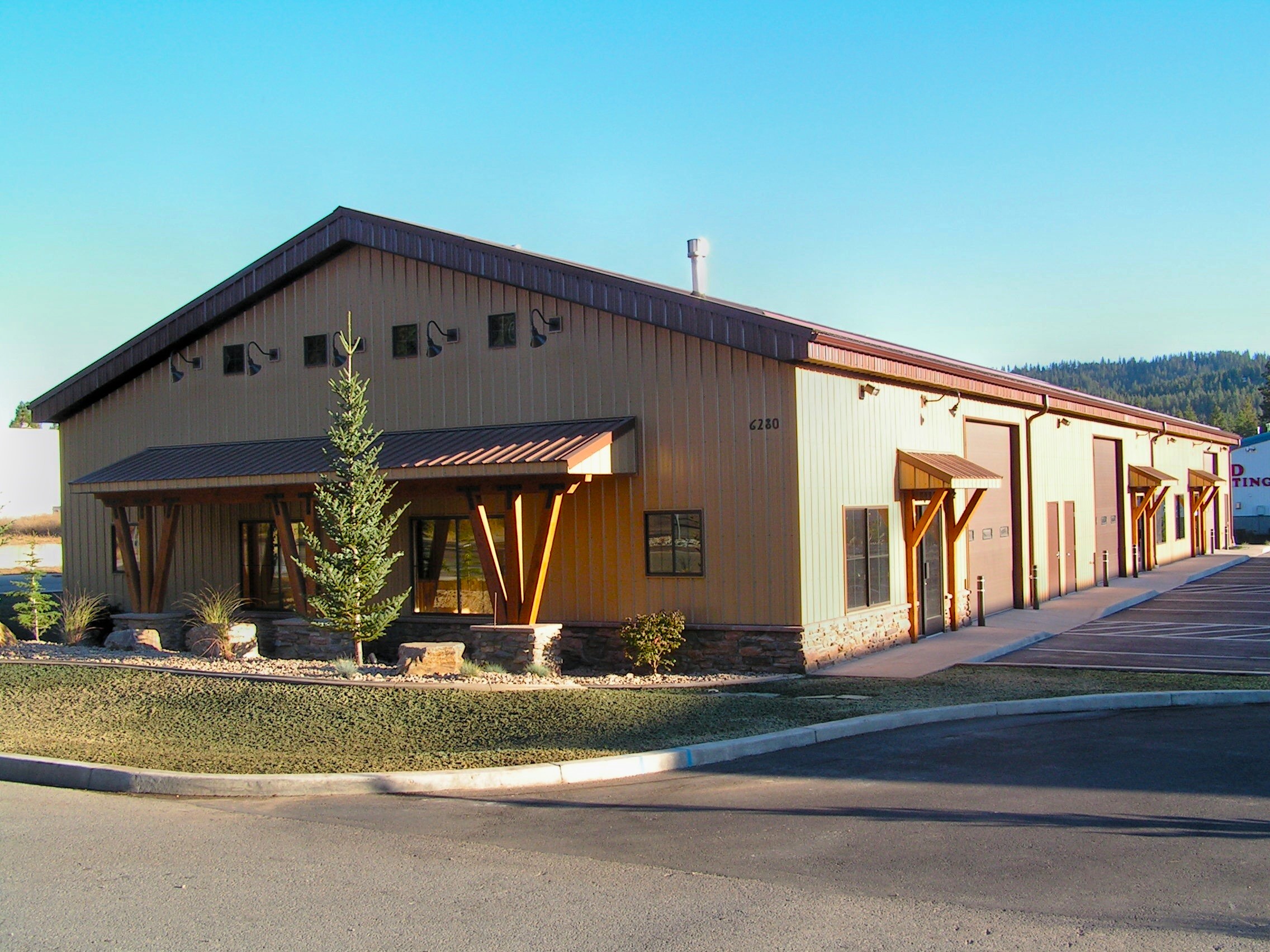 Three unit light industrial steel building with exterior timber frame accents and natural alpine landscaping Post Falls ID