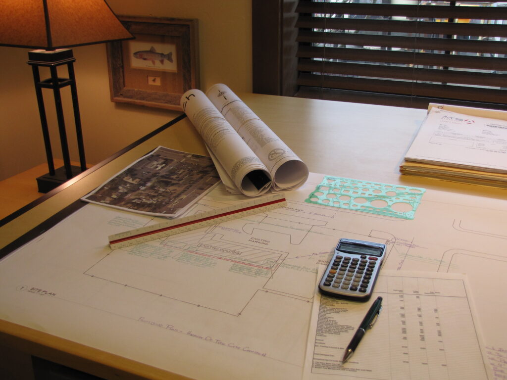 Interior office showing large architectural drafting table covered with blueprints and budget information