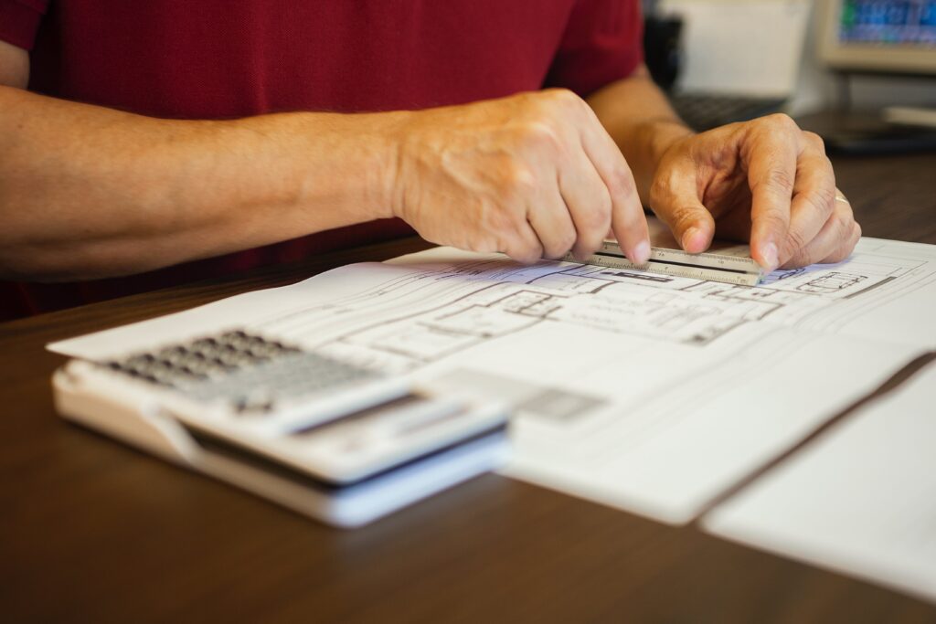 Project manager going over plan schematics and using calculator for budgeting estimates